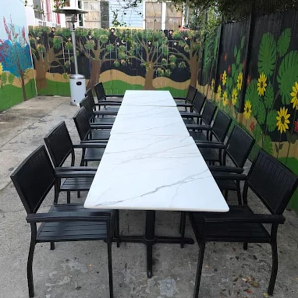 Long outdoor dining table with black chairs and a mural of trees and sunflowers on the fence.