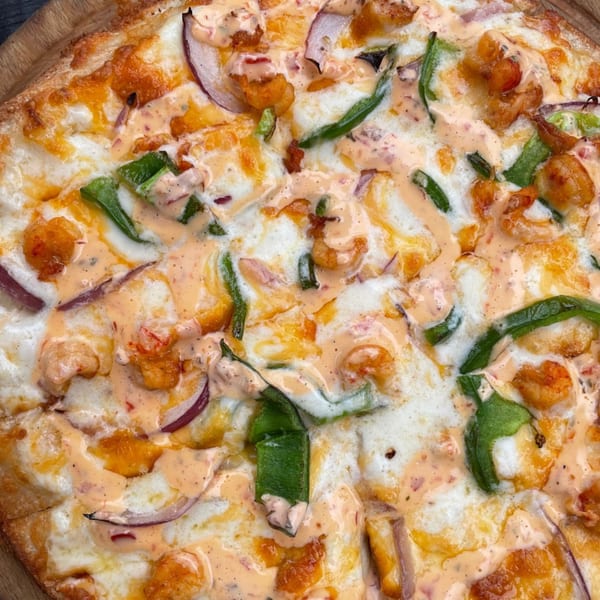 Close-up of a G's Pizza with shrimp, green peppers, red onions, and a creamy orange sauce.