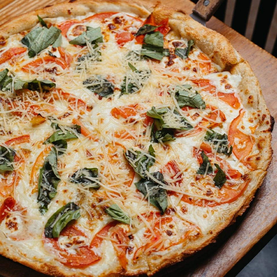 G's Pizza Margherita pizza with fresh tomatoes, basil, and shredded cheese on a wooden peel.