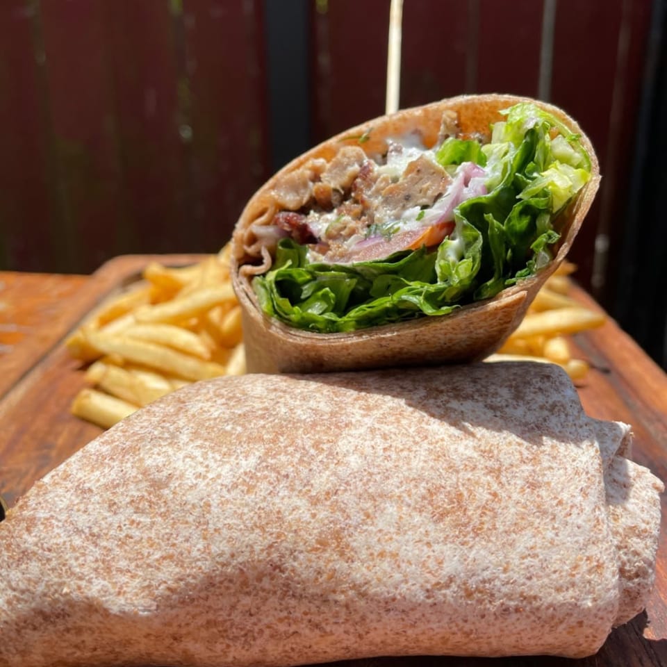 A meat-filled wrap with lettuce and creamy sauce served alongside golden fries on a wooden table.