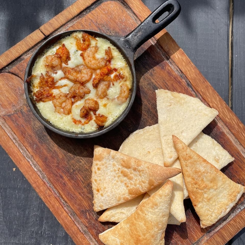 Skillet of cheesy shrimp dip with toasted tortilla triangles on a wooden serving board.