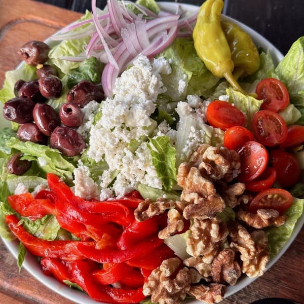 A vibrant G's Pizza salad with lettuce, olives, feta, red onions, tomatoes, peppers, and walnuts.