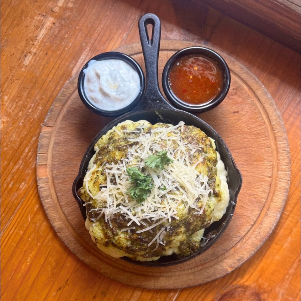 G's Pizza's baked cauliflower with pesto, parmesan, and two dipping sauces on a wooden board.